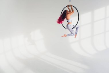 Genç Kızıl saçlı kadın beyaz bir arka plan üzerinde hava ringde akrobatik öğeleri gerçekleştirir.