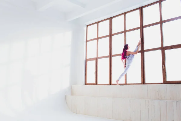 Mooie vrouw doet yoga en acrobatiek in de buurt van het grote raam. — Stockfoto