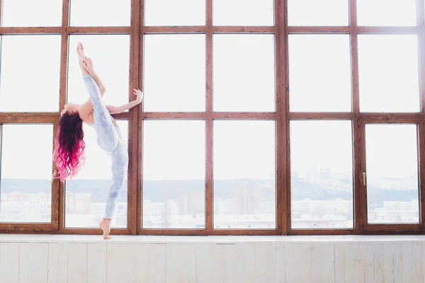 Hermosa mujer haciendo yoga y acrobacias cerca de la gran ventana . — Foto de Stock