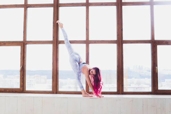 Gyönyörű nő csinál jóga és akrobatika mellett a nagy ablak. — Stock Fotó