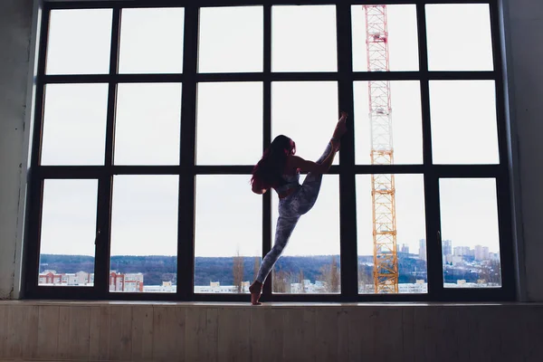 Mooie vrouw doet yoga en acrobatiek in de buurt van het grote raam. — Stockfoto