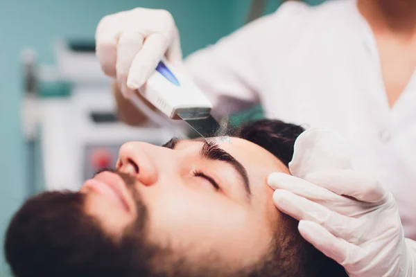 Ultrasonic face cleaning. Young caucasian man, cosmetology.