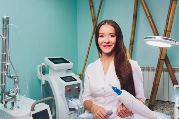 Schöne Kosmetikerin in medizinischen Handschuhen zeigt ihren Arbeitsplatz, blickt in die Kamera und lächelt. — Stockfoto