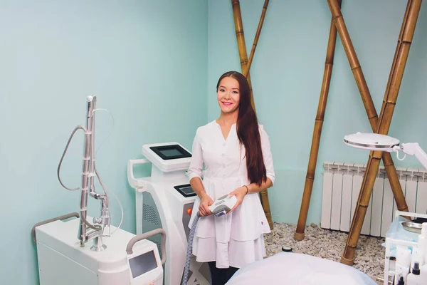 Schöne Kosmetikerin in medizinischen Handschuhen zeigt ihren Arbeitsplatz, blickt in die Kamera und lächelt. — Stockfoto