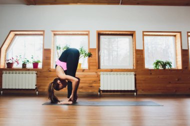 Tanımlanamayan genç bir kadın Yoga egzersiz yapıyor-Padahastasana beyaz duvarlar ile spor salonunda bir halı üzerinde. Metin için Yerleştir.