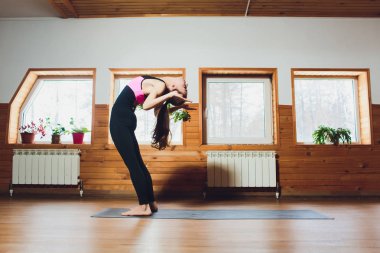 Pratik yoga, diz, uttanasana egzersiz, ayakta ön viraj poz kafa yapıyor, çalışma dışarı, spor giyim, siyah pantolon ve bluz, kapalı tam uzunlukta, yoga Studio gri duvar giyen genç kadın.