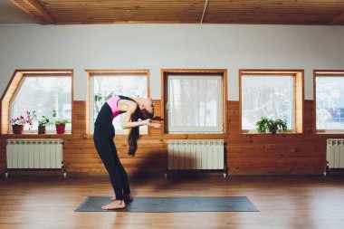 Spor giyim, kapalı tam uzunlukta, beyaz loft studio arka plan yıprattı çalışan pratik yoga, kafa varyasyon diz egzersiz, elleri arkadan uttanasana poz duran genç kadın