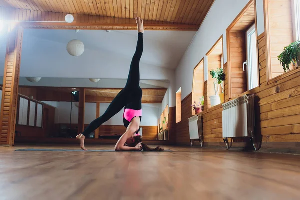 Junge Yogi attraktive Frau praktiziert Yoga-Konzept, steht in Salamba Sirsasana-Übung, Kopfstand-Pose, trainiert, trägt Sportbekleidung, schwarzes Tank-Top und Hose, volle Länge, Loft-Hintergrund. Stockbild