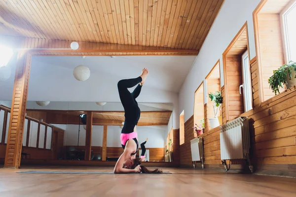 Junge Yogi attraktive Frau praktiziert Yoga-Konzept, steht in Salamba Sirsasana-Übung, Kopfstand-Pose, trainiert, trägt Sportbekleidung, schwarzes Tank-Top und Hose, volle Länge, Loft-Hintergrund. lizenzfreie Stockbilder