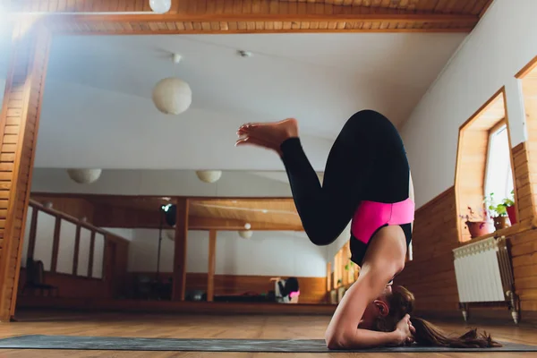 Junge Yogi attraktive Frau praktiziert Yoga-Konzept, steht in Salamba Sirsasana-Übung, Kopfstand-Pose, trainiert, trägt Sportbekleidung, schwarzes Tank-Top und Hose, volle Länge, Loft-Hintergrund. Stockfoto