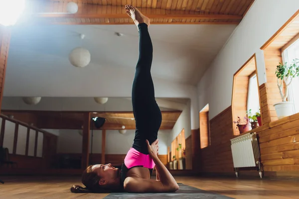 Junge, sportliche attraktive Frau praktiziert Yoga, macht Salamba Sarvangasana-Übungen, unterstützt Schulterstand-Pose, trainiert, trägt Sportbekleidung, Hose und Top, Indoor-Nahaufnahme, weißes Yogastudio. lizenzfreie Stockfotos