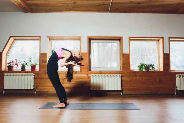 Junge attraktive Frau praktiziert Yoga zu Hause Konzept, steht in uttanasana Übung, Kopf-zu-Knie-Pose, trainieren, trägt schwarze Sportbekleidung, Innen Nahaufnahme Bild, Studio-Hintergrund. Stockbild