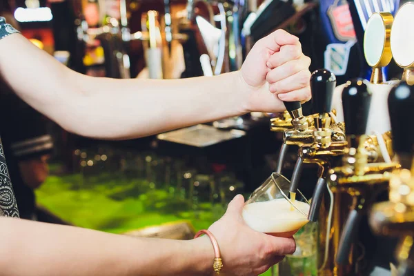 Oktoberfest karşılaştık. Barmen büyük lager bira dokunun içinde dökme el. İstemci için bira döküyor. Yan genç barmen barda bira dururken dökme görünümünü sayaç.