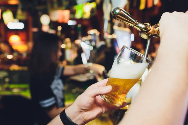 Oktoberfest karşılaştık. Barmen büyük lager bira dokunun içinde dökme el. İstemci için bira döküyor. Yan genç barmen barda bira dururken dökme görünümünü sayaç.