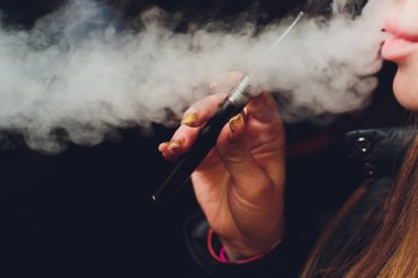 Genç güzel esmer kadın sigara, vaping e-sigara dumanlı siyah arka plan üzerine.