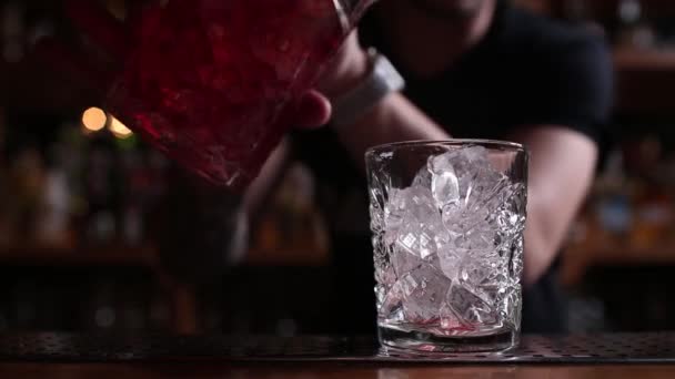 Le mani di Barman cospargono il succo nel bicchiere da cocktail pieno di bevanda alcolica sullo sfondo scuro . — Video Stock