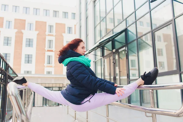 Girl doing exercises on the street. Young woman sit on twine.