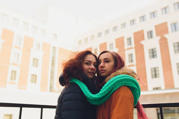 Um casal de jovens lésbicas. Menina usa chapéu quente menina fecha amigos orelhas com as mãos em mitenes no inverno frio . — Fotografia de Stock