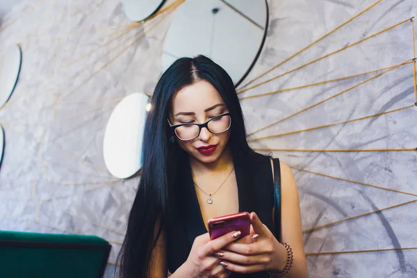 Menina árabe feliz usando telefone inteligente na parede de tijolo. Mulher sorridente com penteado encaracolado em roupas casuais em fundo urbano . — Fotografia de Stock