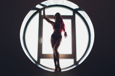 Yuvarlak pencerenin arka planında güzel bir kadının karanlık silueti. yoga, akrobasi.