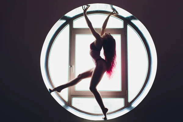 圆形窗户背景上一位漂亮女人的黑暗剪影。瑜伽、杂技. — 图库照片