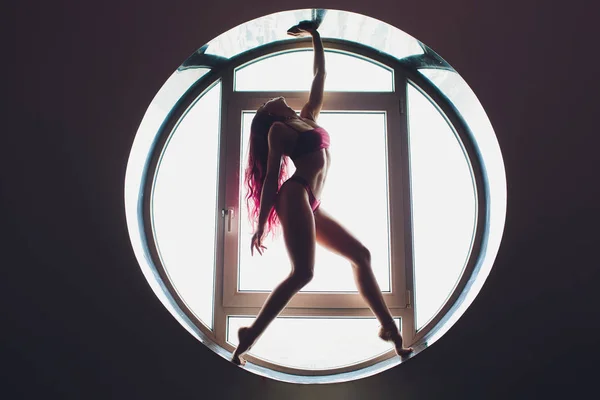 A sötét sziluettje egy gyönyörű nő a háttérben a kerek ablakon. jóga, akrobatika. — Stock Fotó