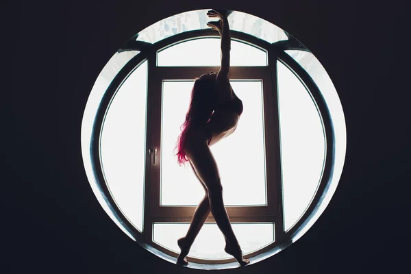 La silueta oscura de una hermosa mujer en el fondo de la ventana redonda. yoga, acrobacias . —  Fotos de Stock