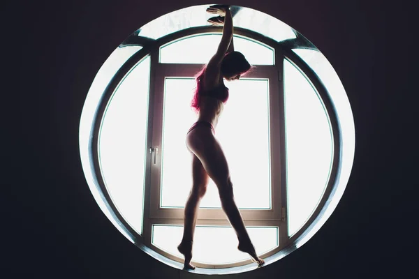 The dark silhouette of a beautiful woman on the background of the round window. yoga, acrobatics. — Stock Photo, Image