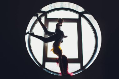 Yuvarlak pencerenin arka planında çocuklu güzel bir kadının karanlık silueti. yoga, akrobasi.