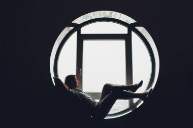 Bir pencerede oturan genç adam şehre bakıyor. Erkekler otel odasının penceresinde güneşlenmeyi severler..