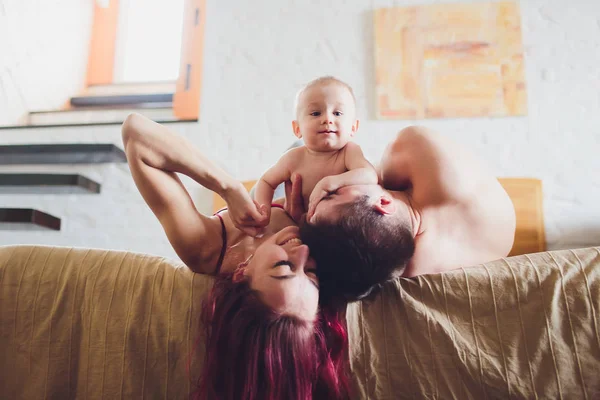 Happy parents with adorable little baby girl sitting on the couch at home, enjoying parenthood, young happy family, new life concept. — Stock Photo, Image