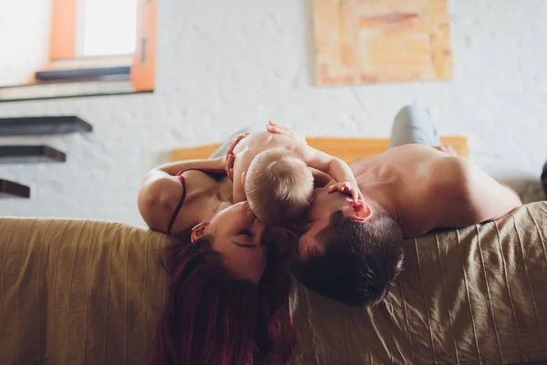 Happy parents with adorable little baby girl sitting on the couch at home, enjoying parenthood, young happy family, new life concept. — Stock Photo, Image