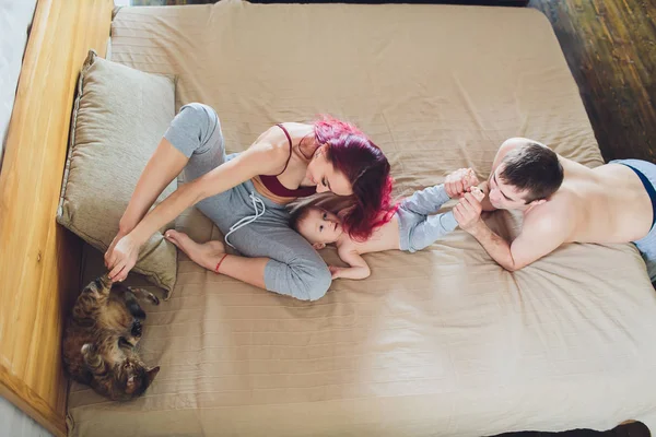 Boldog fiatal szülők-val baba és macska az ágyban otthon. — Stock Fotó