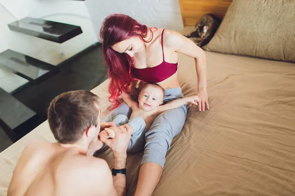 Boldog fiatal szülők babával az ágyban otthon. — Stock Fotó