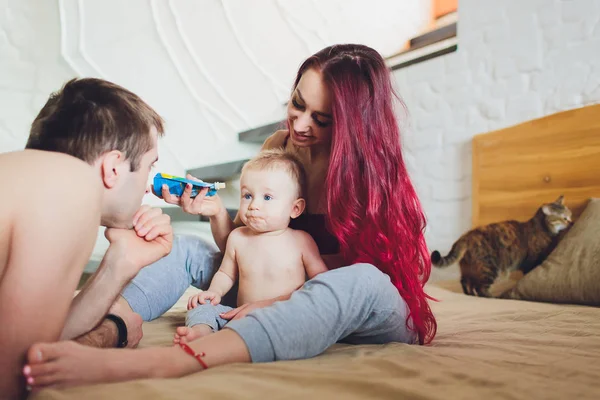 Padres jóvenes felices con el bebé en la cama en casa . —  Fotos de Stock