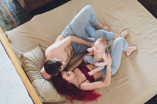 Pais jovens felizes com bebê na cama em casa . — Fotografia de Stock