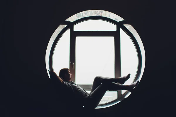 Young man sitting in a window looking out over the city . Men enjoy sun in window of hotel room. — ストック写真