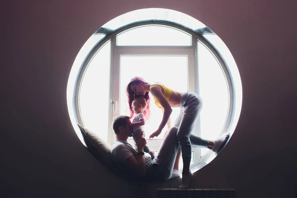 Счастливая семья из матери, отца и маленького сына играет и обнимается дома на полу у большого окна . — стоковое фото