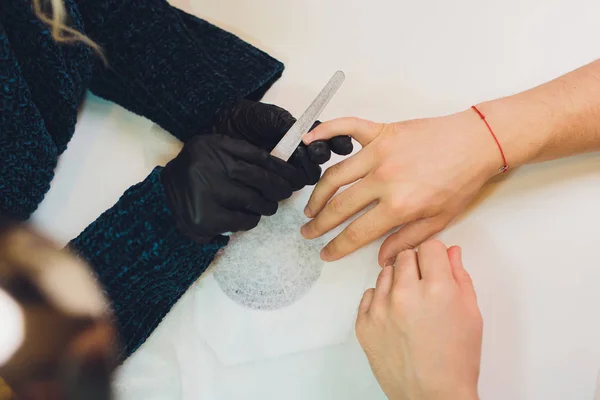 Hände in Handschuhen kümmern sich um die Nägel der Hände. Schönheitssalon für Maniküre. — Stockfoto