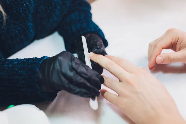 Hände in Handschuhen kümmern sich um die Nägel der Hände. Schönheitssalon für Maniküre. — Stockfoto