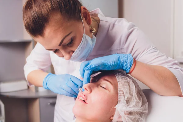 Il cosmetologo medico fa procedura di aumento del labbro di una bella donna in un salone di bellezza.. — Foto Stock