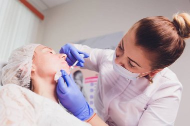 Doktor Kozmetolog, bir güzellik salonunda güzel, Genç bir kadının yüz derisi üzerinde kırışıklıkları sıkma ve yumuşatma için yüz enjeksiyonları prosedürü yapar. Kozmetoloji Cilt Bakımı.