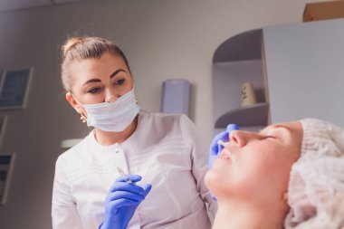 Doktor Kozmetolog, bir güzellik salonunda güzel, Genç bir kadının yüz derisi üzerinde kırışıklıkları sıkma ve yumuşatma için yüz enjeksiyonları prosedürü yapar. Kozmetoloji Cilt Bakımı.
