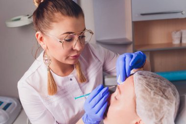 Doktor Kozmetolog, bir güzellik salonunda güzel, Genç bir kadının yüz derisi üzerinde kırışıklıkları sıkma ve yumuşatma için yüz enjeksiyonları prosedürü yapar. Kozmetoloji Cilt Bakımı.