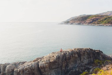 azgın denize karşı bir kaya üzerinde duran bir adamın silueti.