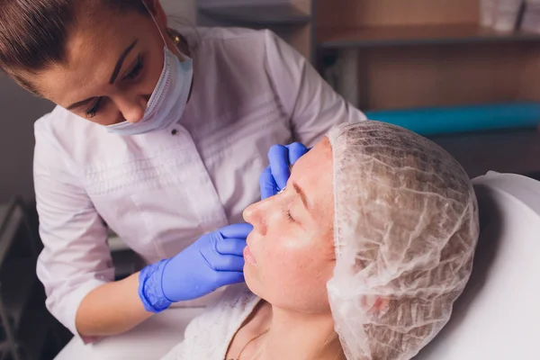 Dokter kosmetolog membuat prosedur injeksi wajah untuk mengencangkan dan merapikan keriput di kulit wajah seorang wanita muda yang cantik di salon kecantikan. Kosmetologi perawatan kulit . — Stok Foto