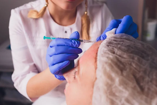 Il medico cosmetologo fa la procedura di iniezioni facciali per stringere e levigare le rughe sulla pelle del viso di una bella, giovane donna in un salone di bellezza. Cosmetologia cura della pelle . — Foto Stock