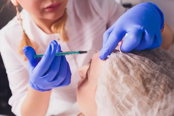 Il medico cosmetologo fa la procedura di iniezioni facciali per stringere e levigare le rughe sulla pelle del viso di una bella, giovane donna in un salone di bellezza. Cosmetologia cura della pelle . — Foto Stock