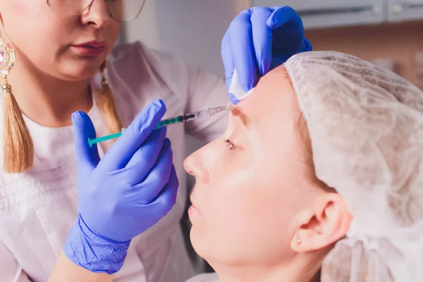 Il medico cosmetologo fa la procedura di iniezioni facciali per stringere e levigare le rughe sulla pelle del viso di una bella, giovane donna in un salone di bellezza. Cosmetologia cura della pelle . — Foto Stock