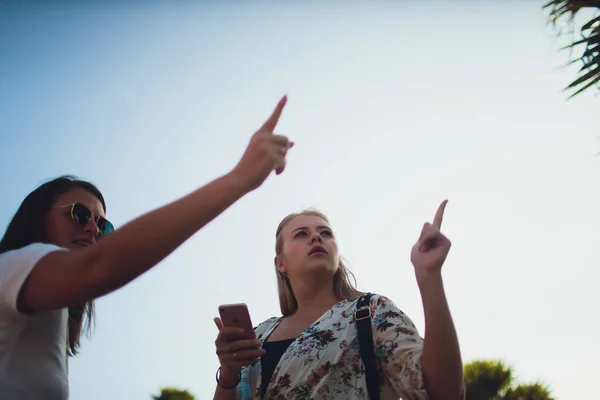 Dos niñas alegres, de pie en la calle con una revista en sus manos, mostrar un dedo. día de verano . — Foto de Stock